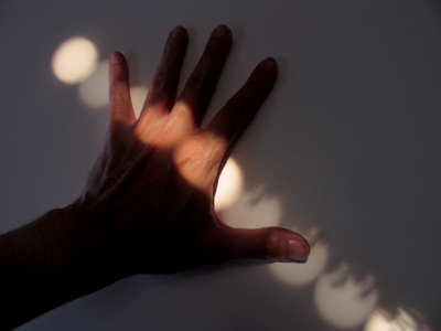 Tiny holes in the window blinds project discs of sunset, including silhouettes of tree branches blowing in the wind.