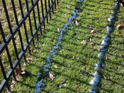 Two thin bands of snow on the ground correspond to the two horizontal bars in the fence.
