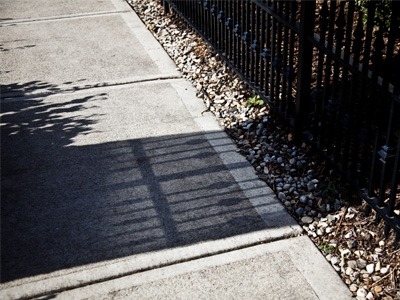 The sun on the left cast a shadow of the tree.  It also reflected off a window on the right, which cast another shadow of the fence on top of the tree shadow.