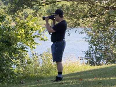 A guy with a big camera taking pictures of birds.  This could be a self-portrait, except for details like the socks.